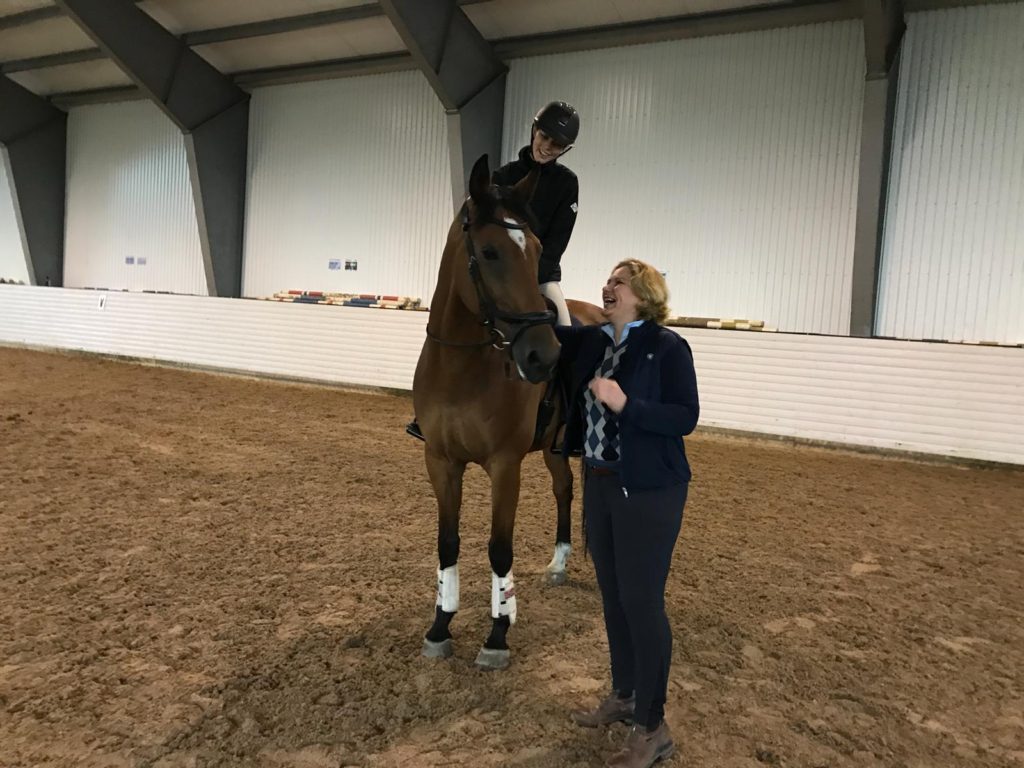 Girl on brown horse with trainer in arena