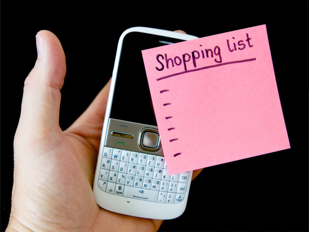 Hand holding phone and sticky note shopping list