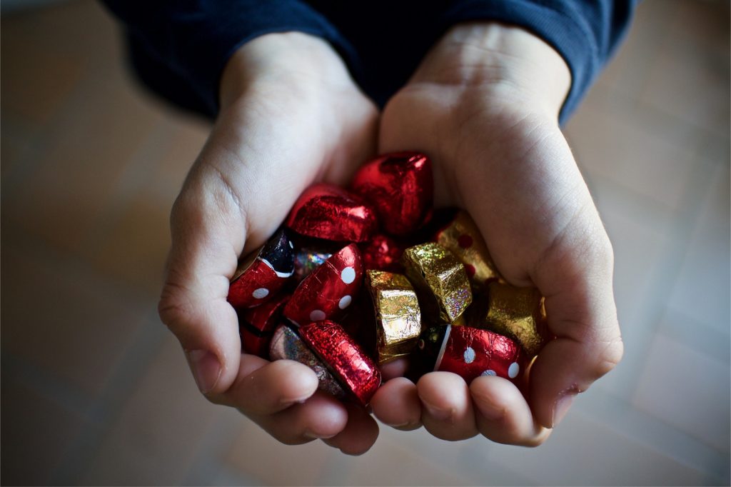 Two hands forming a heart and holding red and gold candy. Candy as stocking stuffer.
