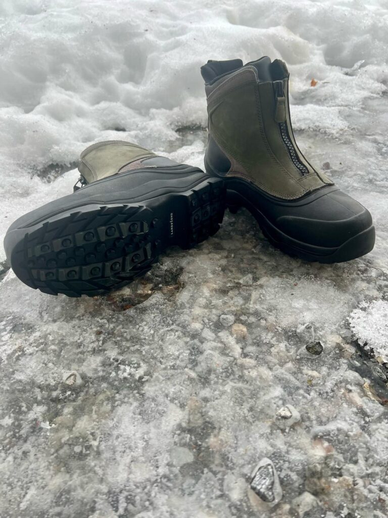 Pair of winter boots with zippers, one standing on ice, one flat